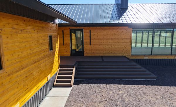Modern wooden building with a sloped metal roof, steps, and large windows in a gravel courtyard