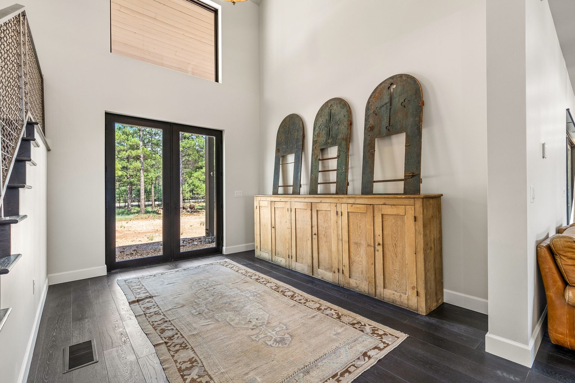Bright entryway with black double doors, wooden cabinet, mirror, and patterned rug on dark wood floors