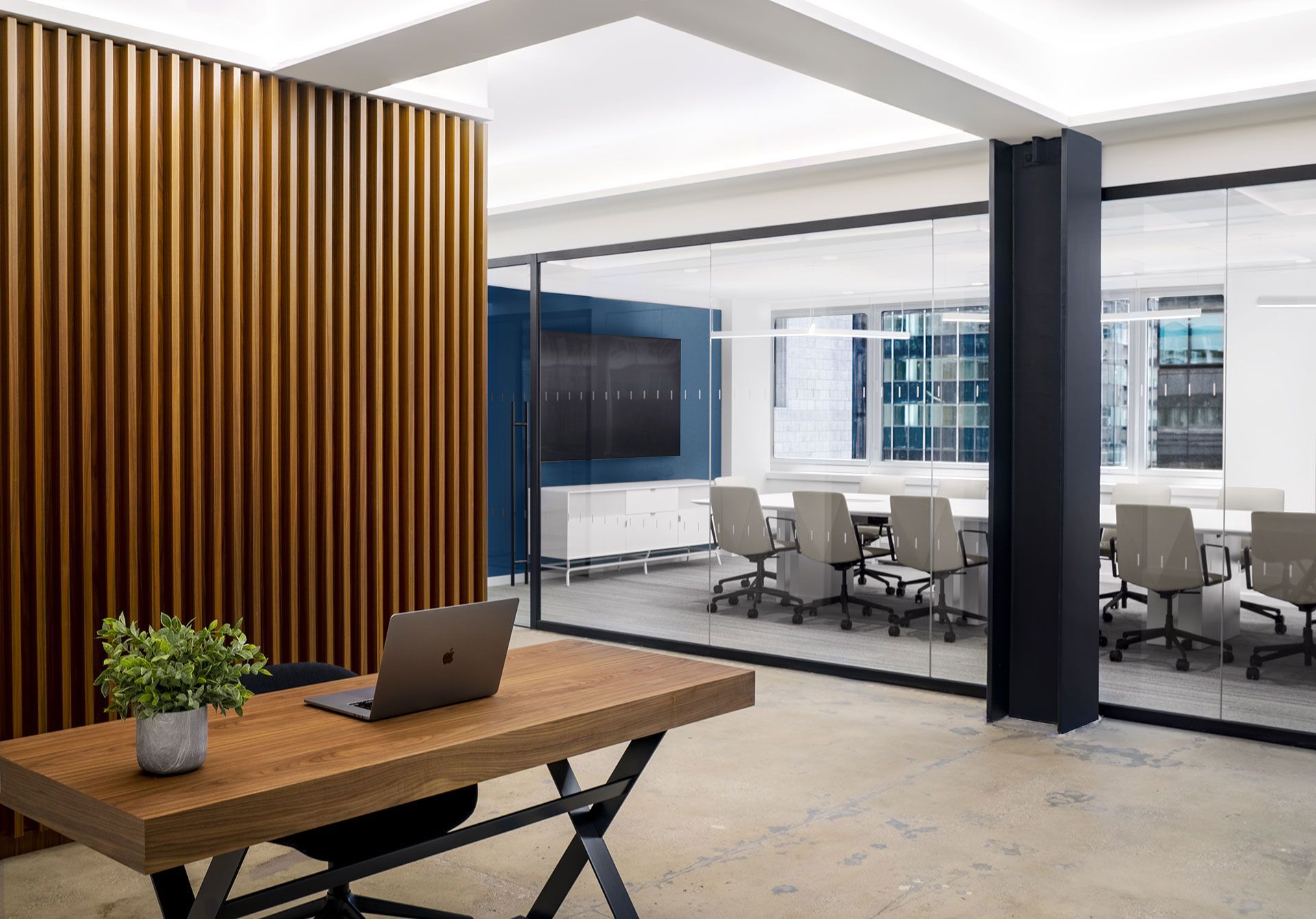 Modern office conference room with glass walls, meeting table, chairs, and a wooden accent wall beside a desk.