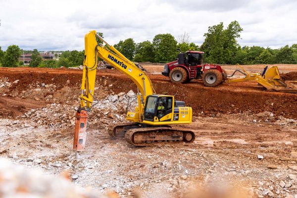 Yellow excavator digging in a muddy construction site, with a tractor and dirt pile in the background
