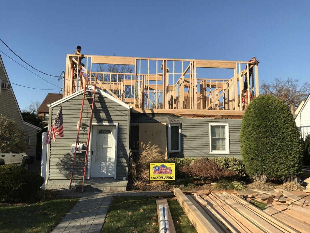 House under construction with new wooden roof framing, ladder, and lumber in the front yard.