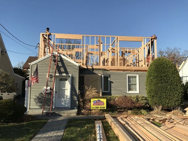 Concrete foundation under construction beside a red brick house with blue safety fencing and dirt piles