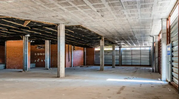 Empty unfinished industrial interior with concrete pillars, exposed ceiling, and large windows