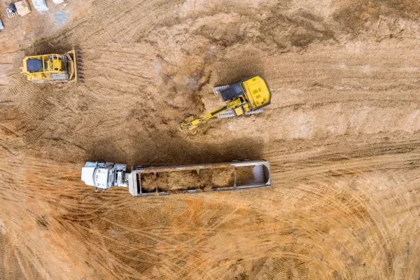 Aerial view of construction site with excavators, dump truck, and a white truck on dirt ground