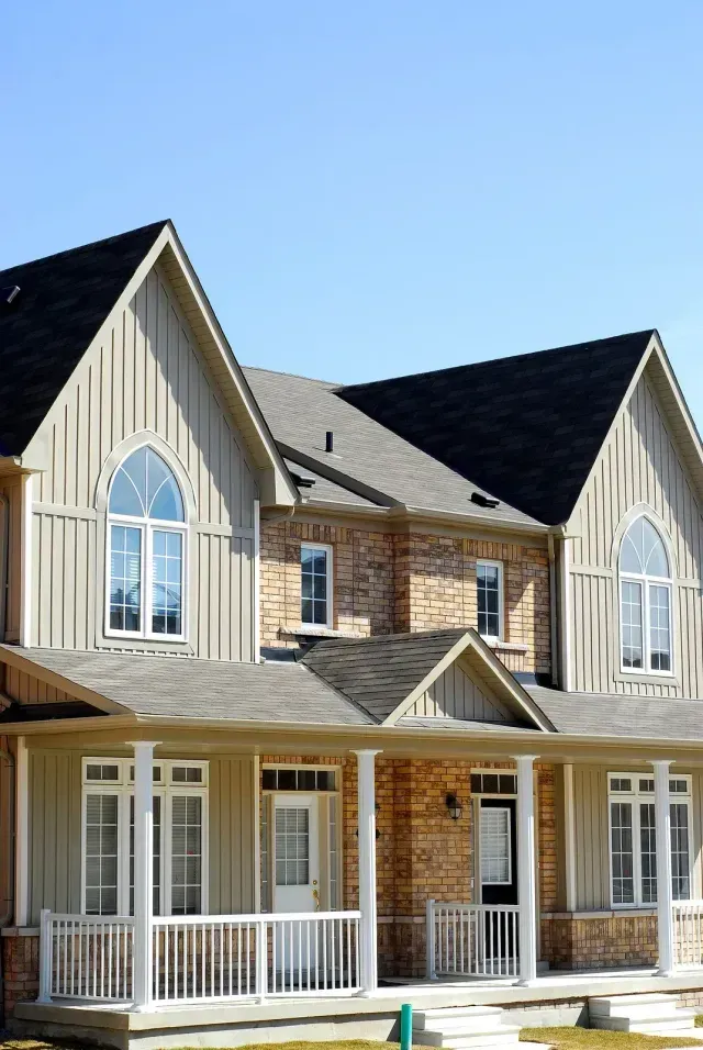 Two-story suburban house with beige siding, brick accents, white porch railings, and arched windows