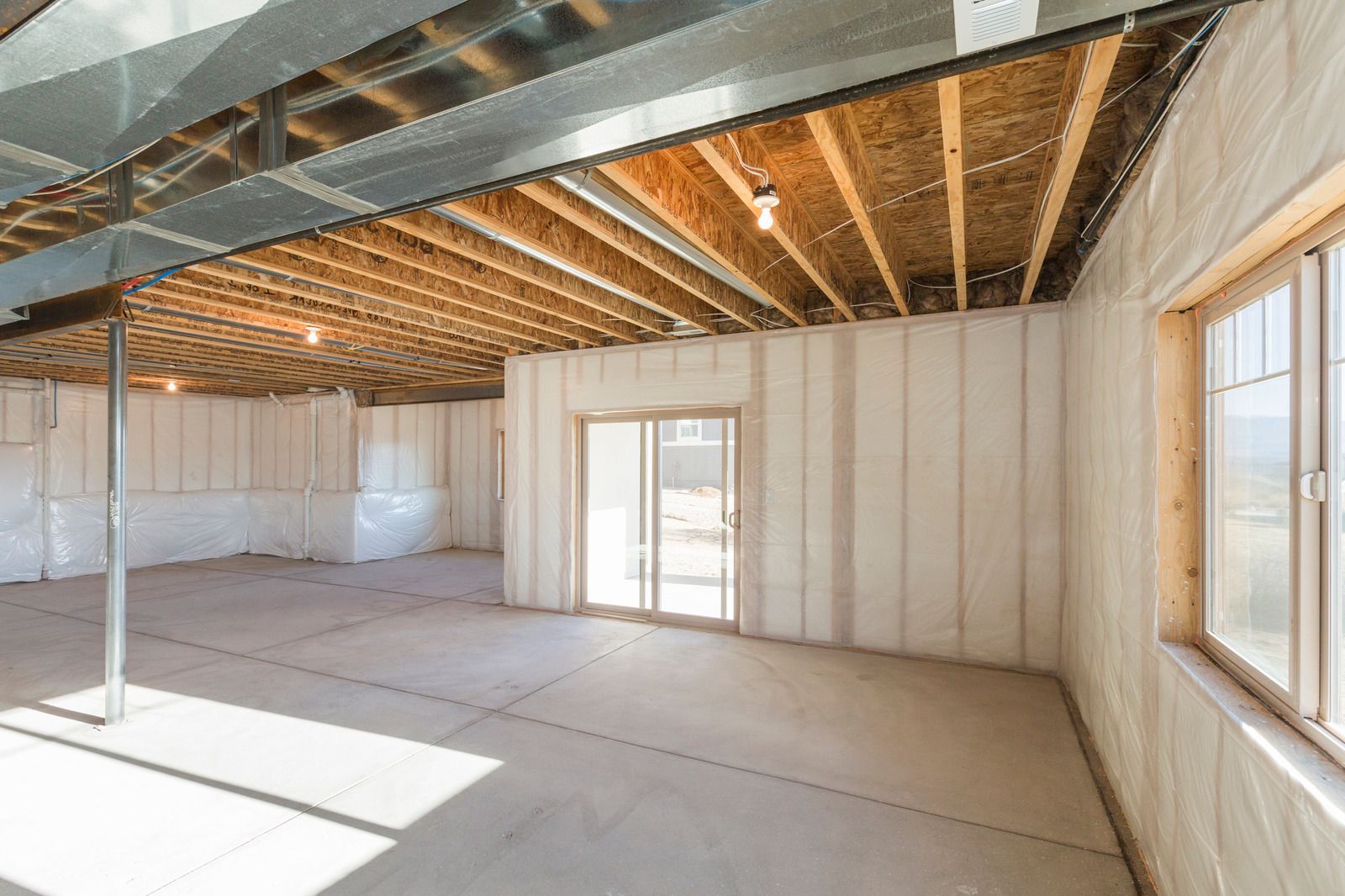 Unfinished room with exposed ceiling beams, drywall walls, and bright windows.