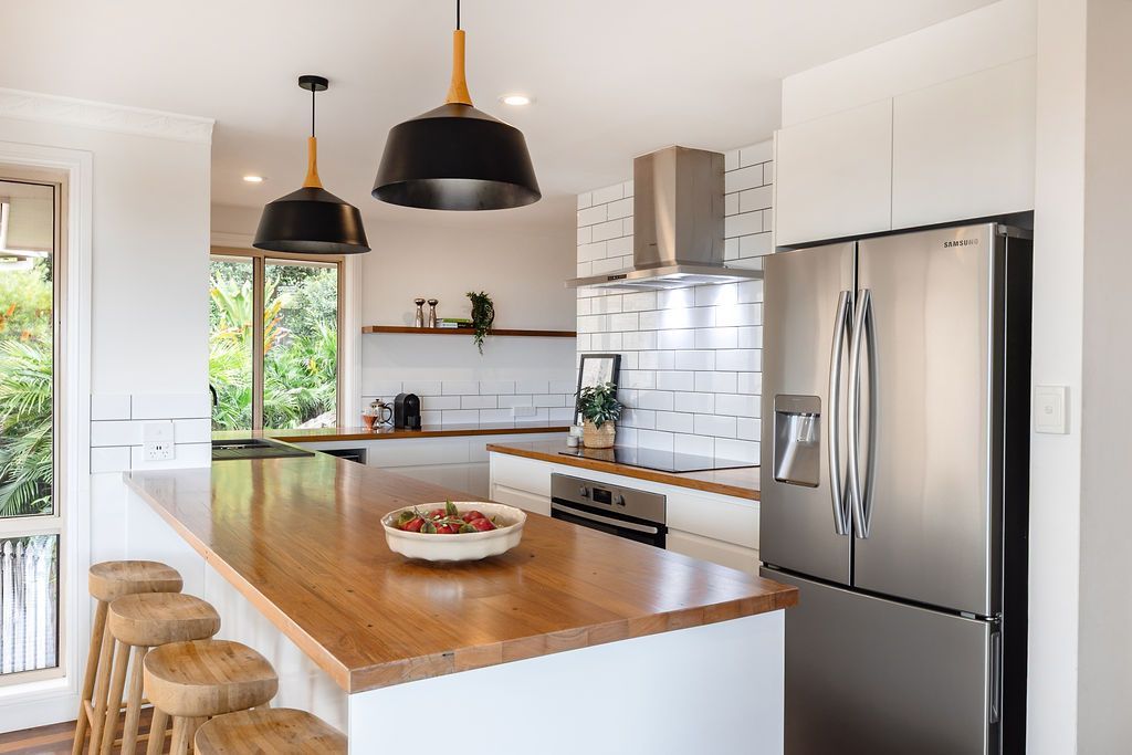 Modern White Kitchen With Wooden Island, Stainless Steel Appliances, and Two Pendant Lights — Flow Kitchens in Taree South, NSW