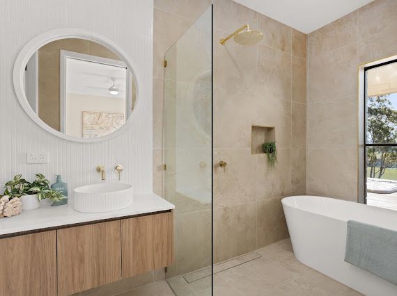 Modern bathroom with a round mirror, wooden vanity, glass shower, and freestanding tub. — Flow Kitchens in Taree South, NSW