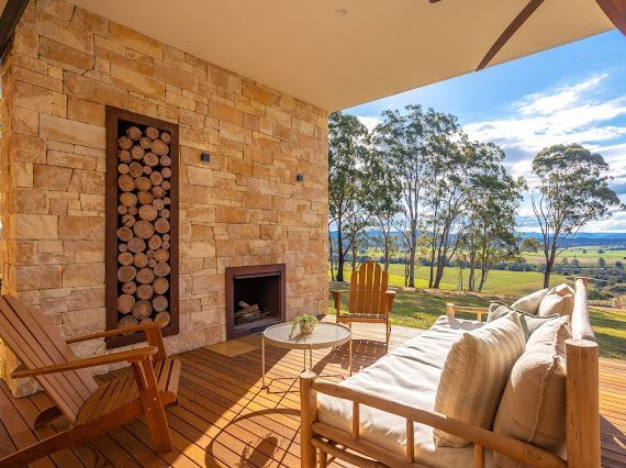 Outdoor Patio With Wooden Furniture, Fireplace, and Firewood Storage, Overlooking a Green Landscape — Flow Kitchens in Taree South, NSW