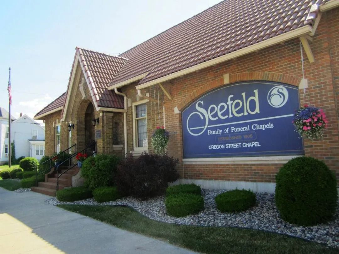 Seefeld Funeral Chapels building with brown brick, blue sign, and flower baskets.
