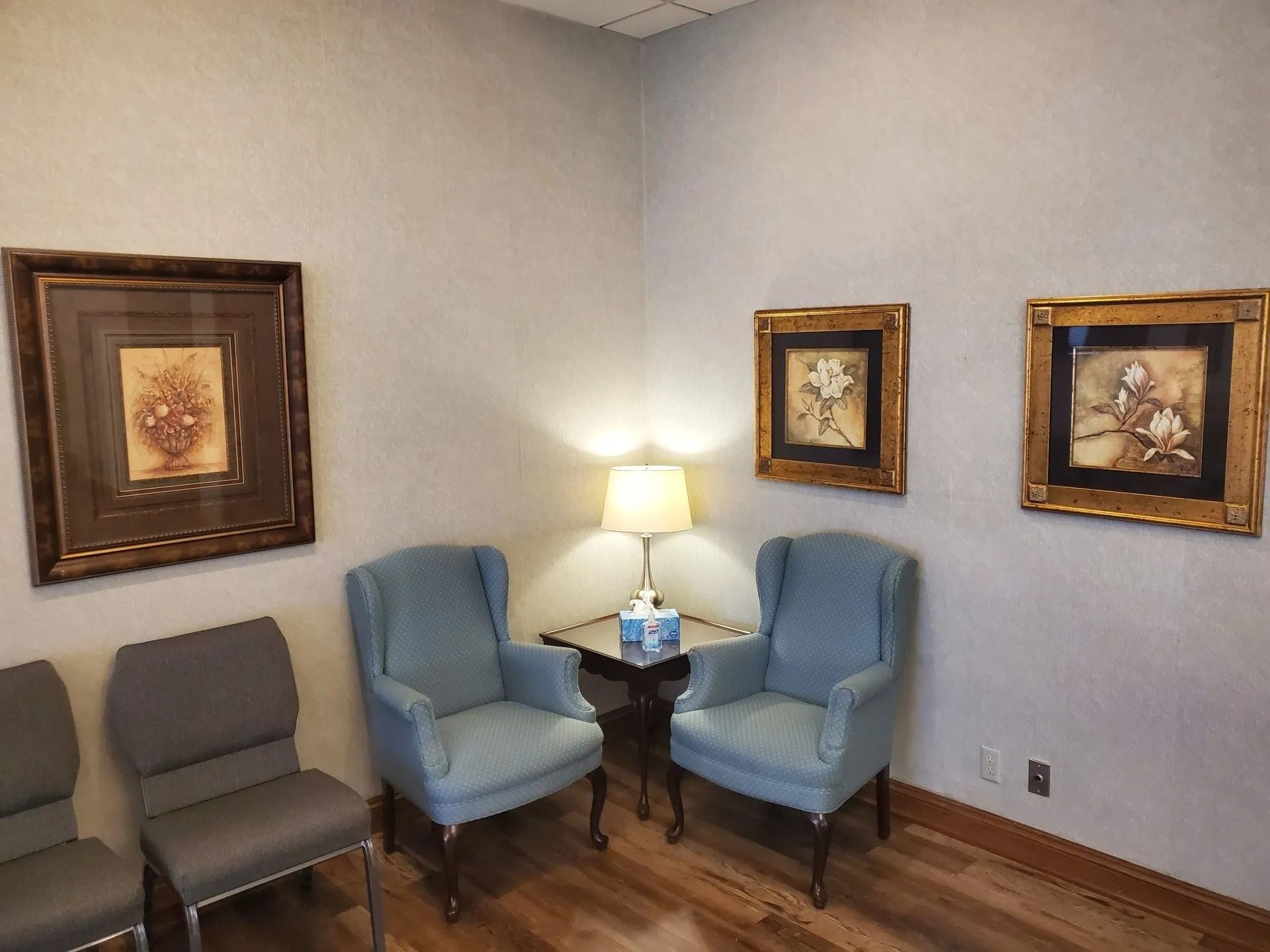 Waiting room with light blue chairs, art, and a table lamp.