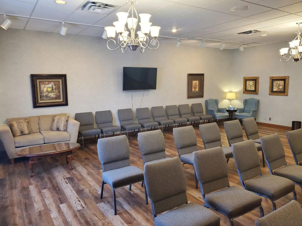 Room with rows of chairs, a couch, and artwork on the walls. There's a TV, chandeliers, and wood-look flooring.