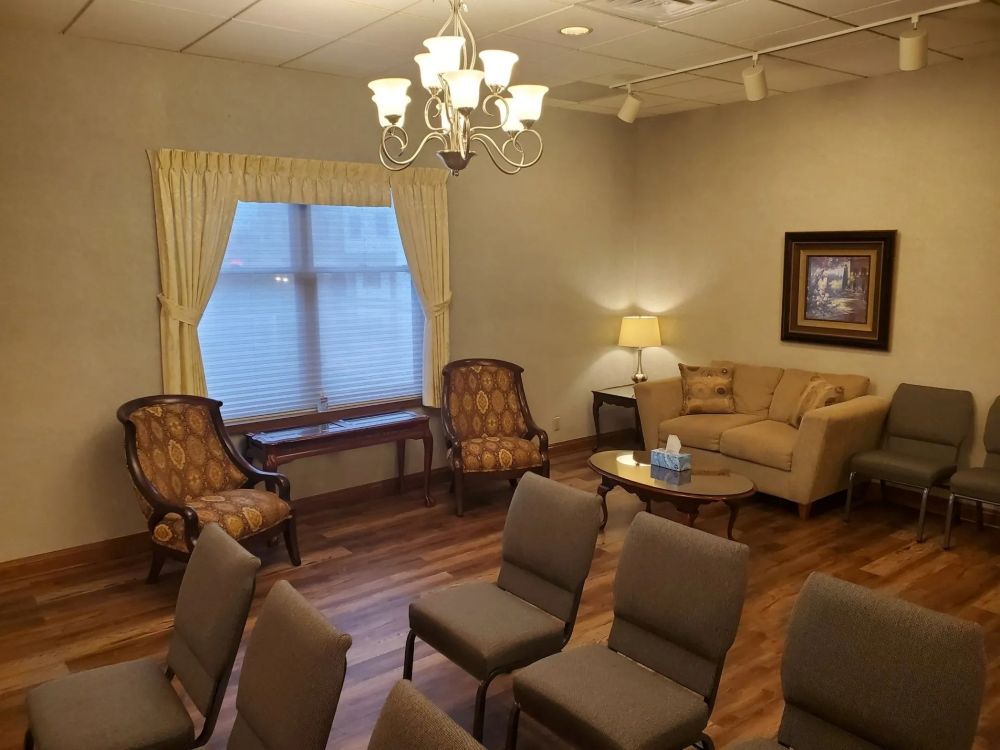 Interior of a room with chairs, a couch, and a window with curtains. Soft lighting and a chandelier.