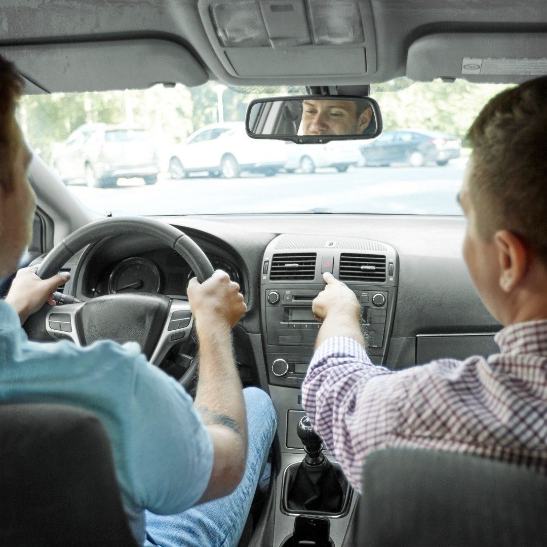 Two men are driving a car and one is adjusting the radio