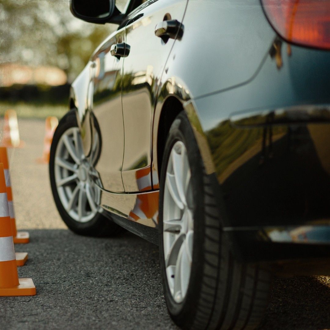 A black car is parked next to a row of orange cones