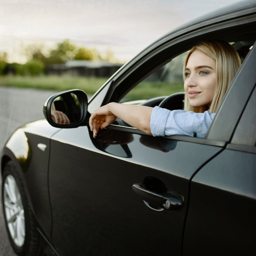 A woman is sitting in a car with her arm out the window