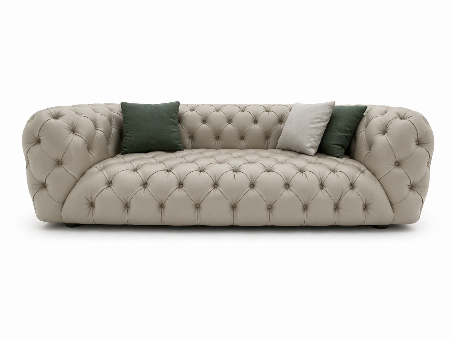 Divano beige trapuntato con braccioli arrotondati e cuscini verde scuro e grigi su sfondo bianco.
