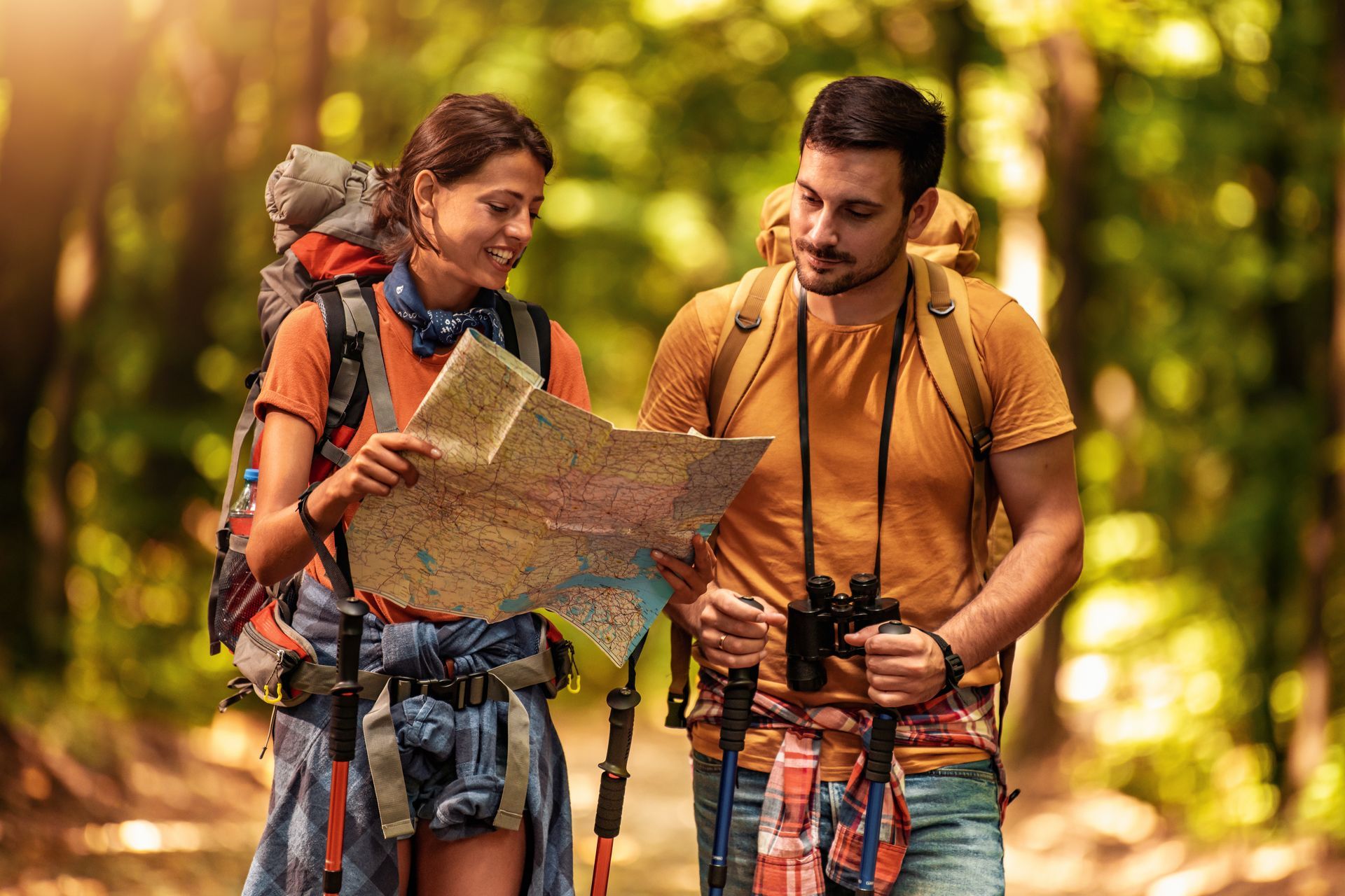 A man and a woman are hiking in the woods and looking at a map.