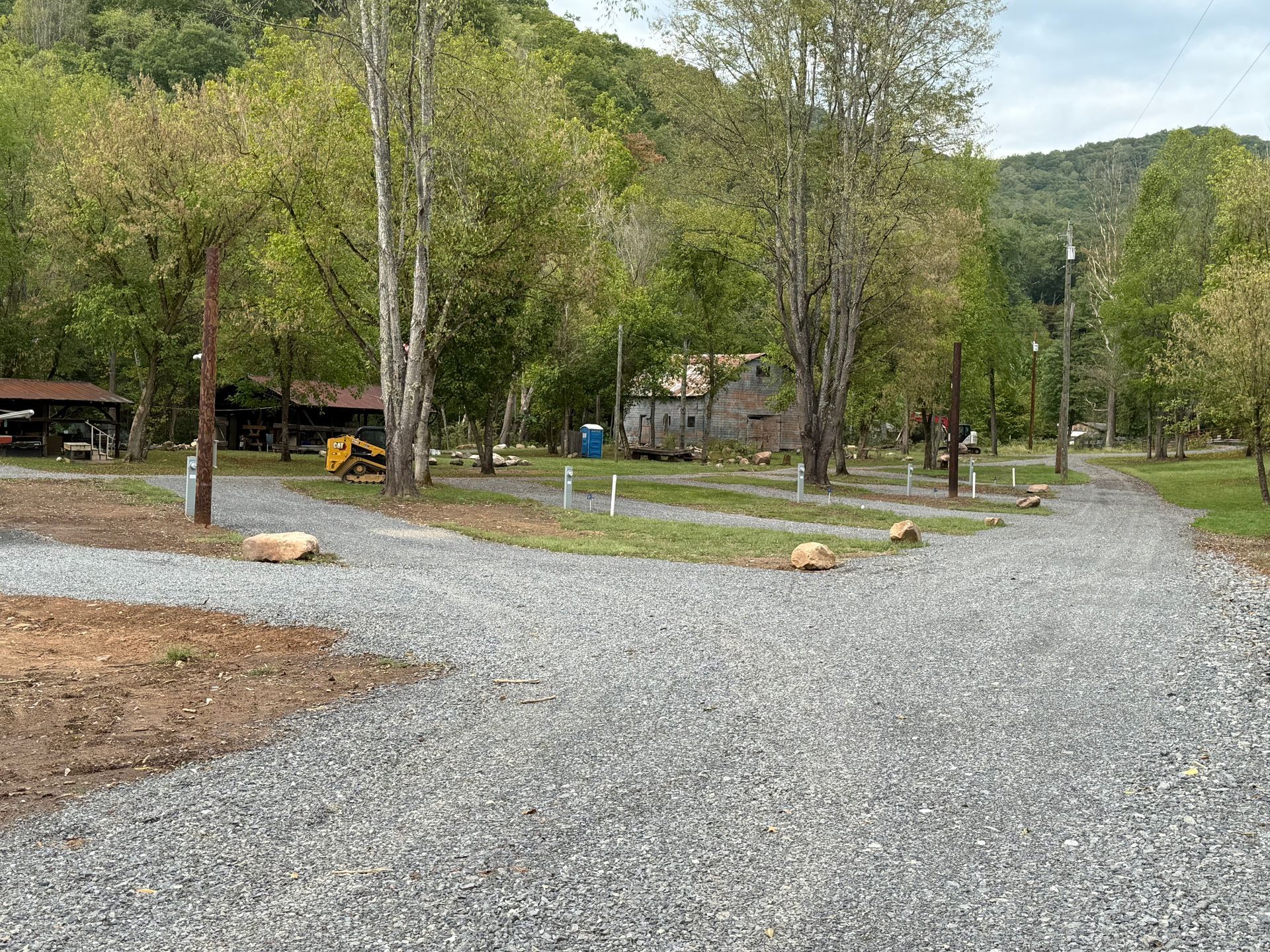 A gravel road going through a park with trees and a house in the background.