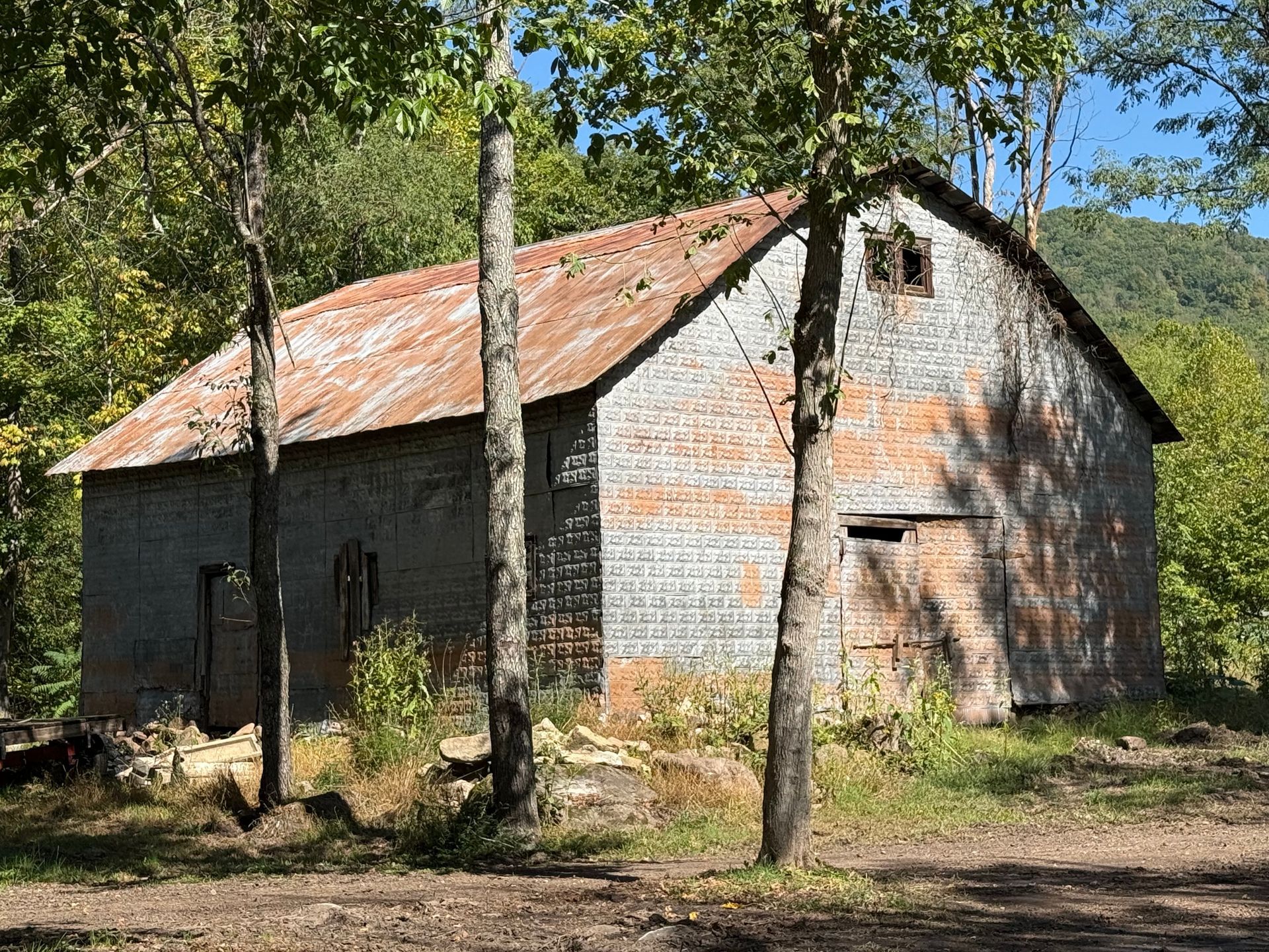 An old brick barn with a tin roof is surrounded by trees.