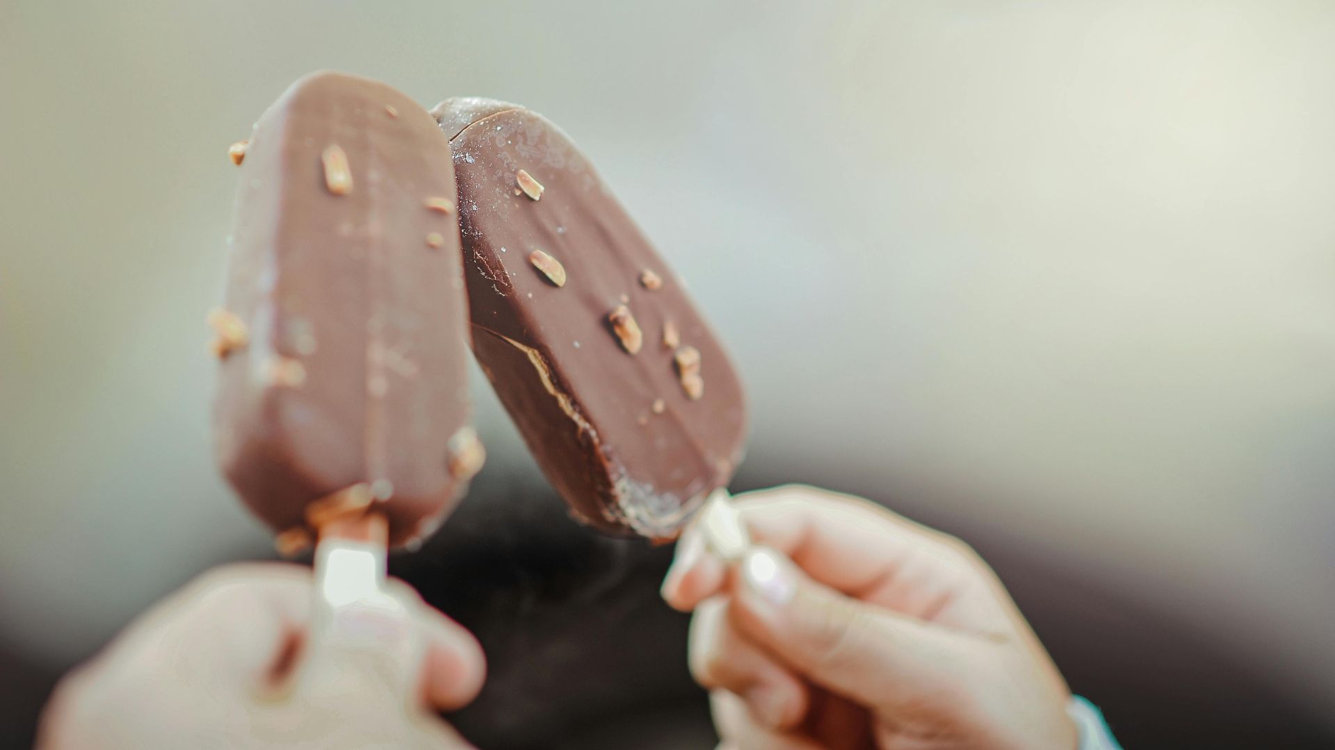 A person is holding two chocolate ice cream bars in their hands.