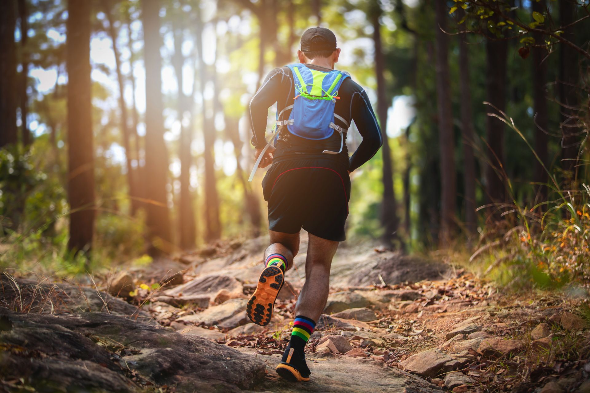 A man with a backpack is running down a trail in the woods.