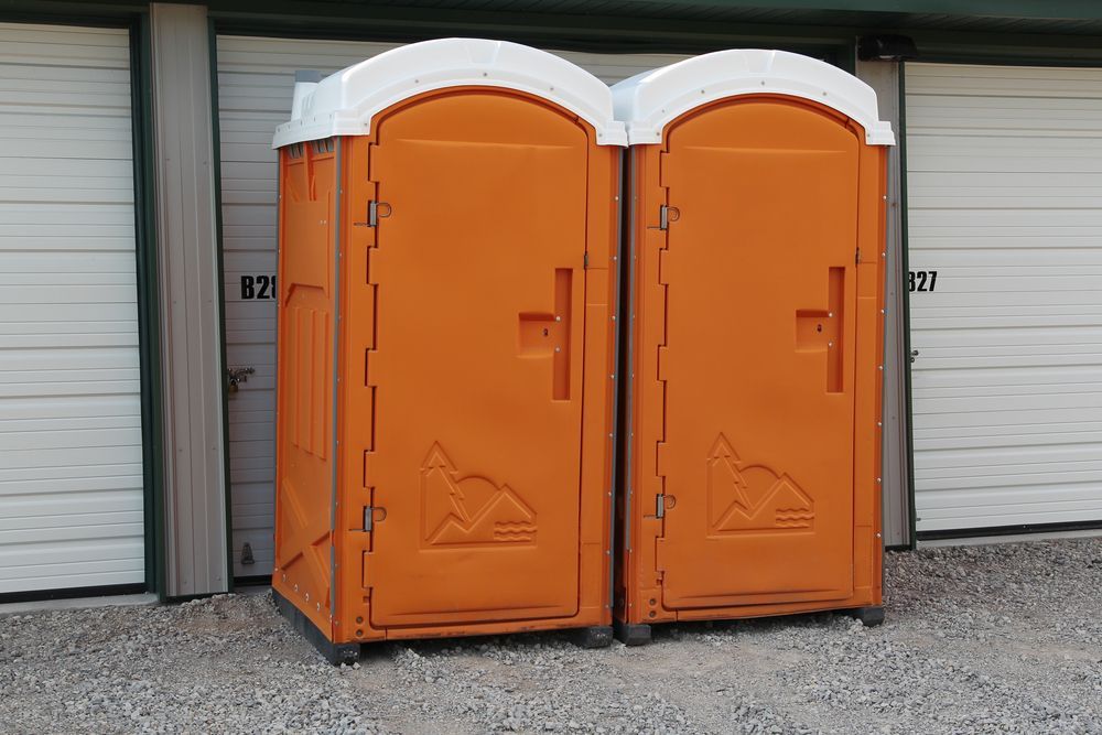 Two orange portable toilets are sitting next to each other in front of a garage door.