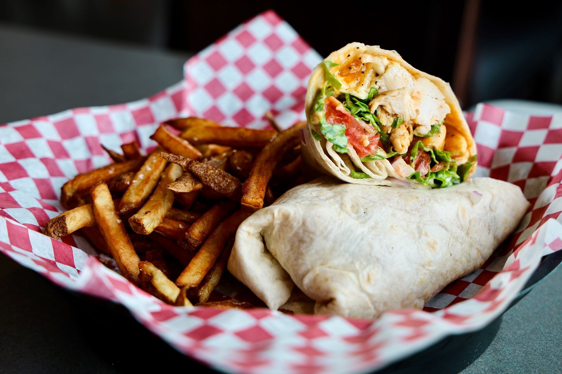 A wrap and french fries on a checkered paper on a table.