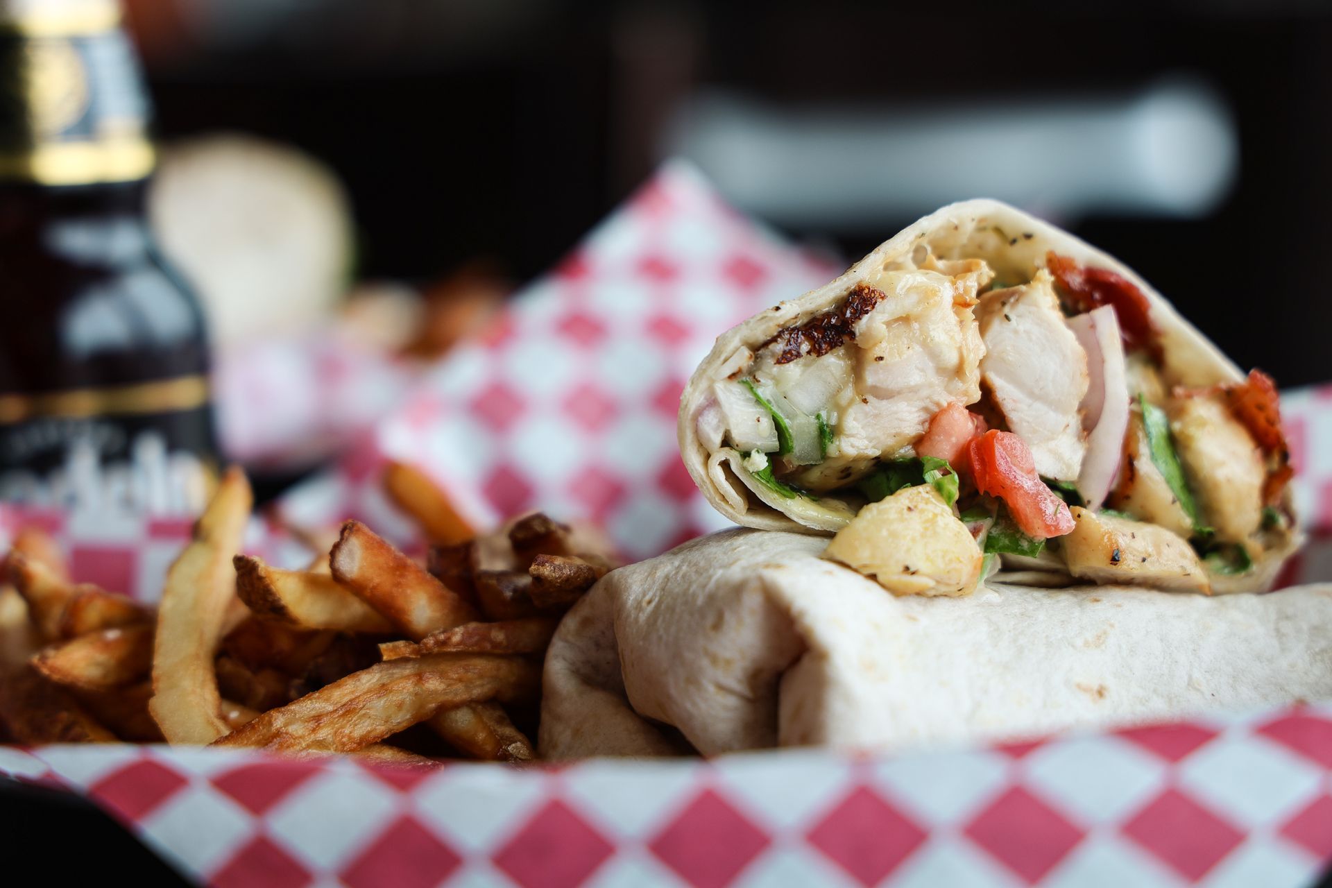 A close up of a wrap and french fries on a checkered paper.