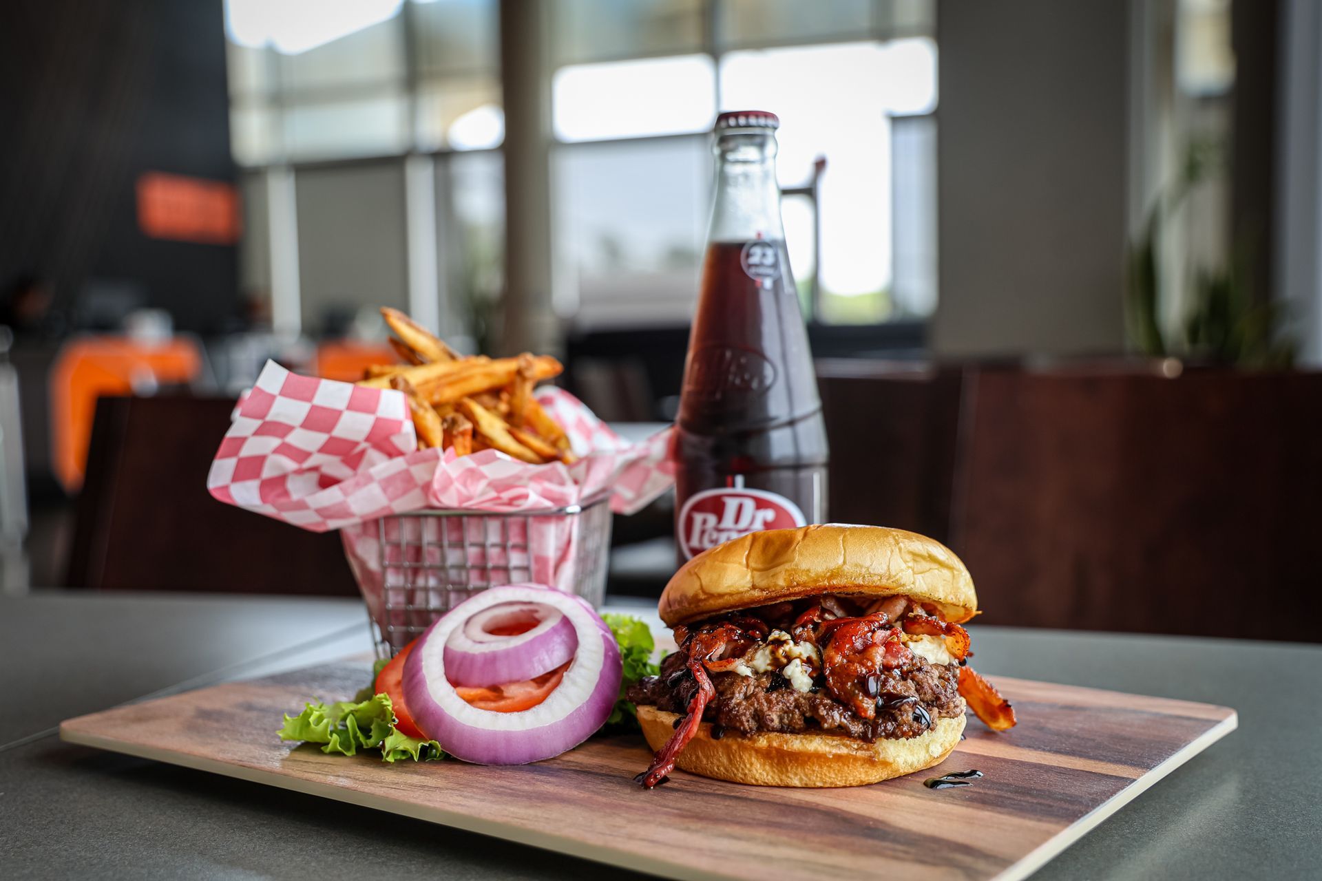 A hamburger and french fries are on a wooden cutting board next to a bottle of soda.