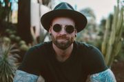 A man wearing a hat and sunglasses is sitting in front of a cactus.
