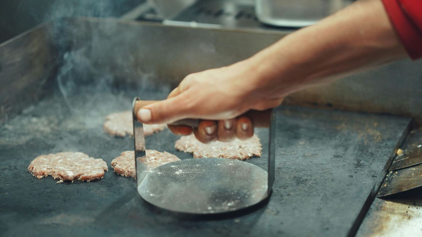 A person is pressing hamburger patties on a grill.