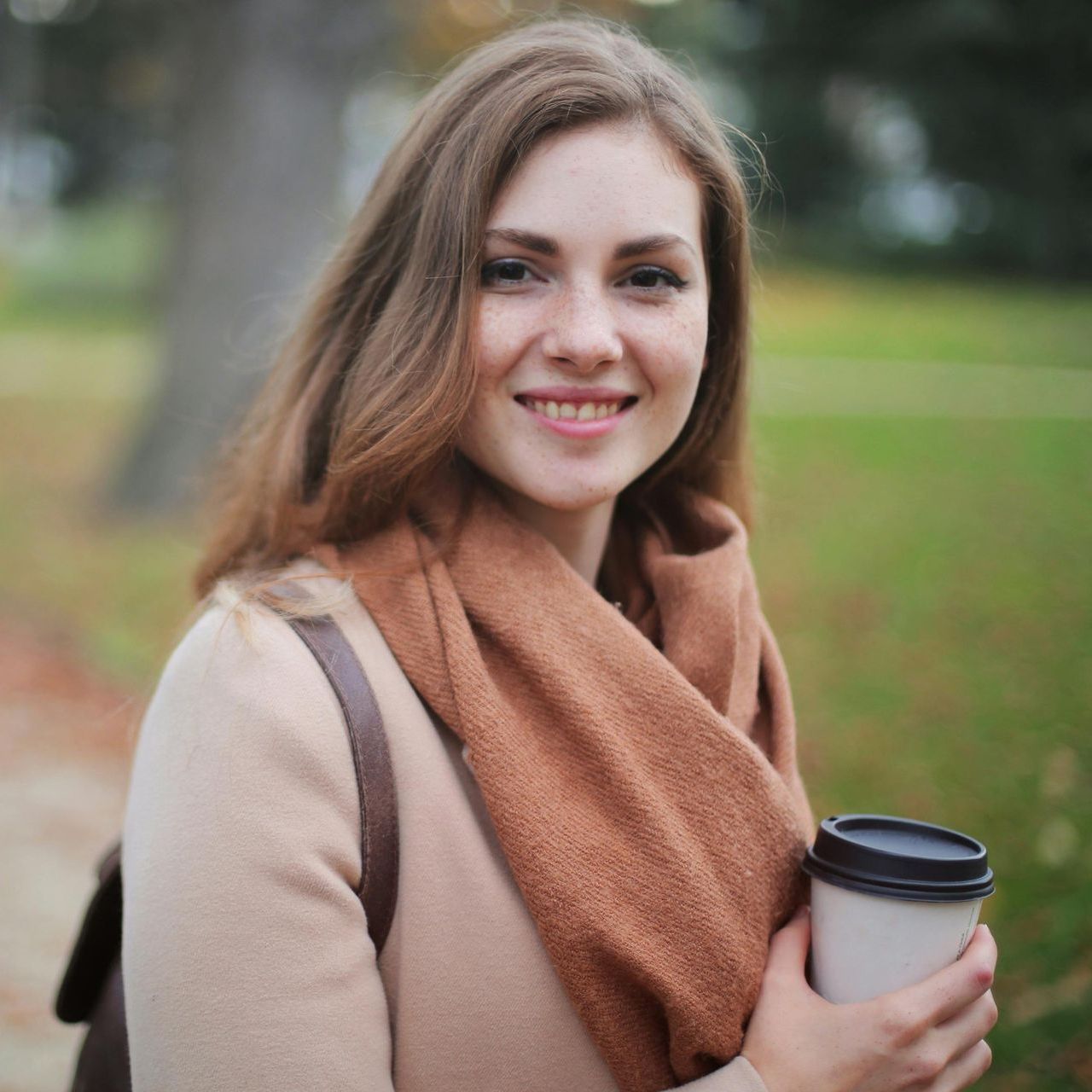 A woman wearing a scarf is holding a cup of coffee