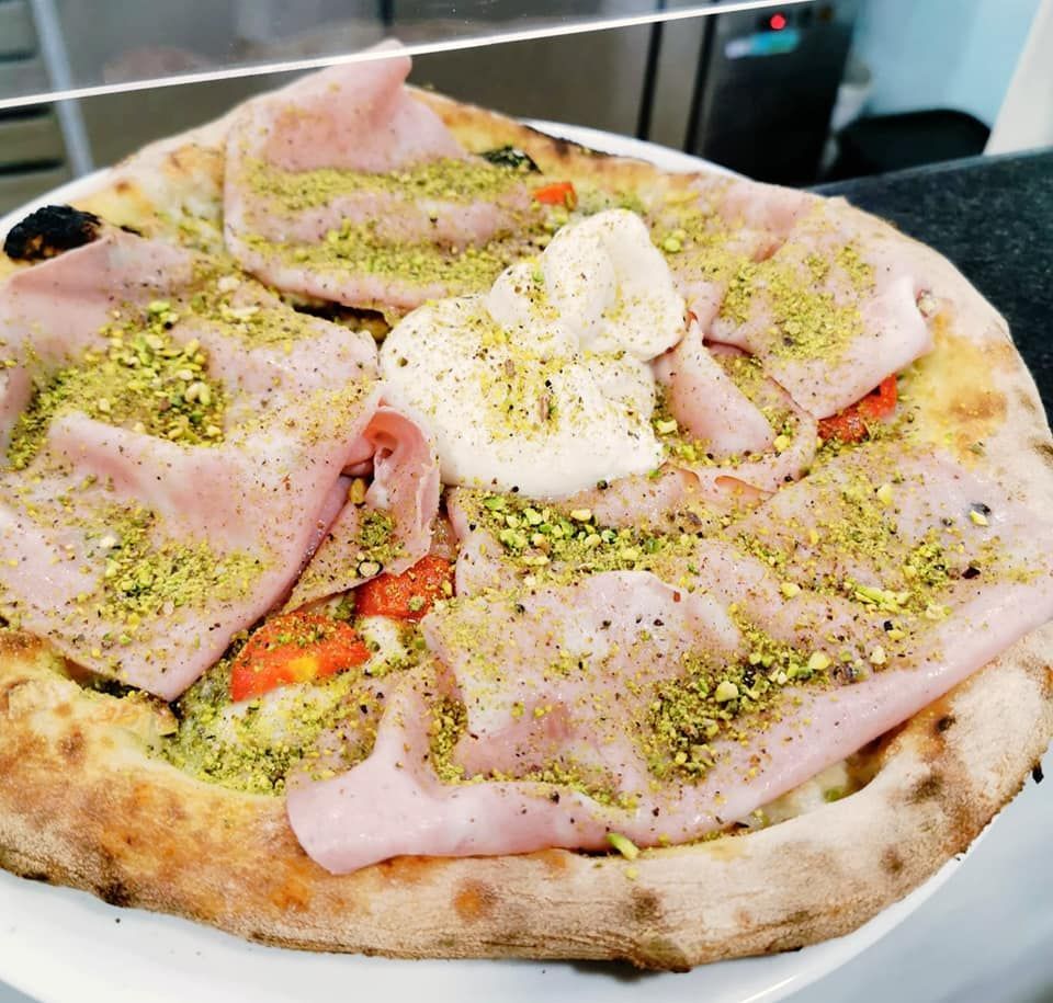 Una pizza con prosciutto e pistacchi su un piatto bianco