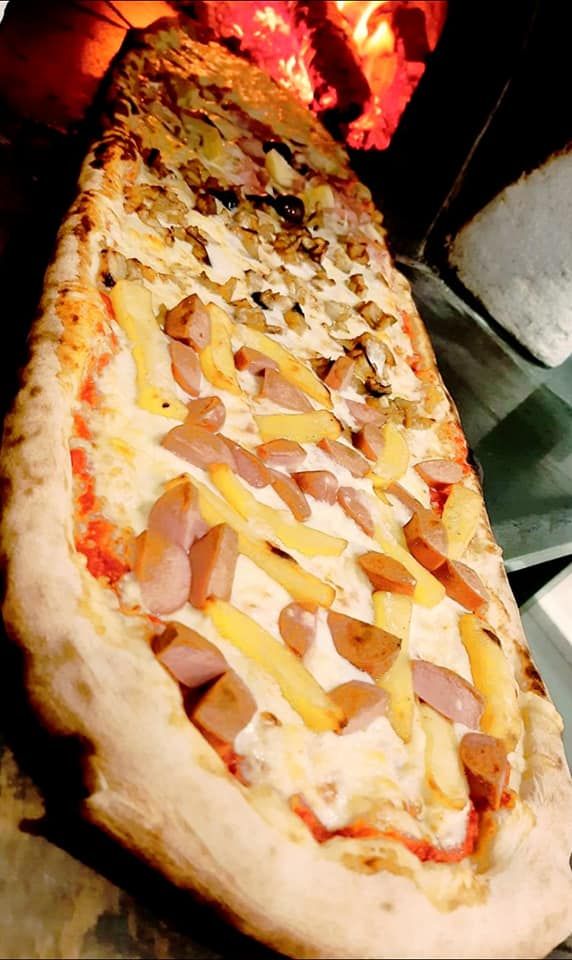 Una pizza lunga con patatine fritte e salsiccia è appoggiata su un tavolo.