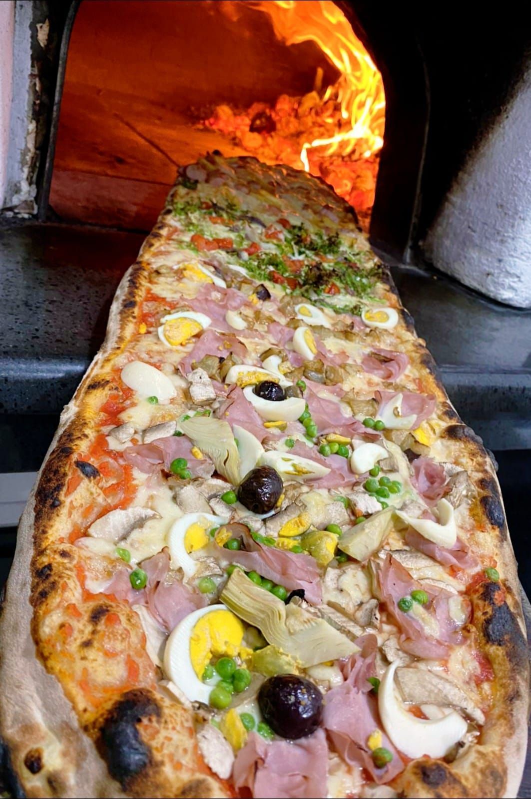 Una pizza molto lunga con molti condimenti viene cotta nel forno.