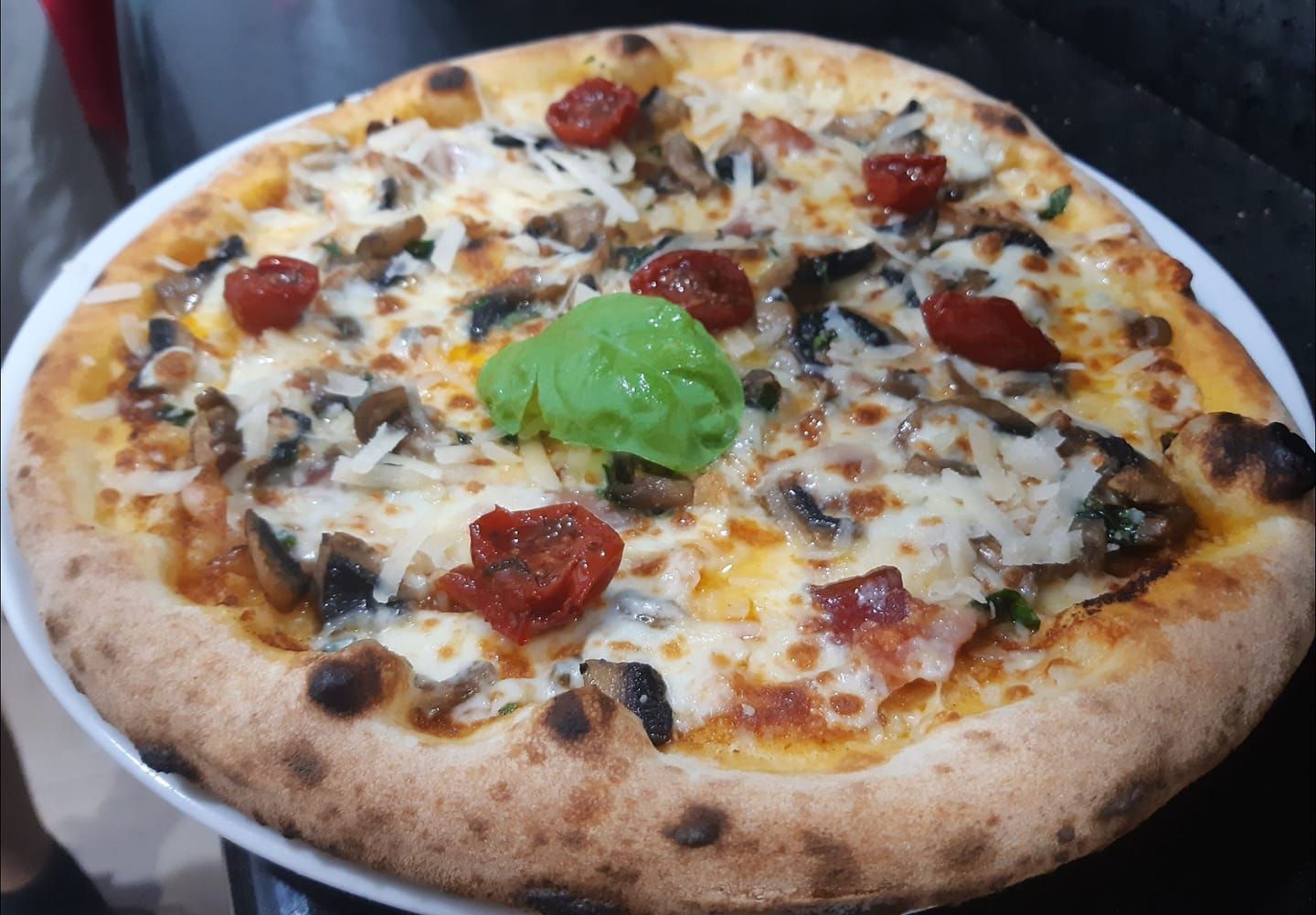 Una pizza con funghi, pomodori e basilico su un piatto bianco.