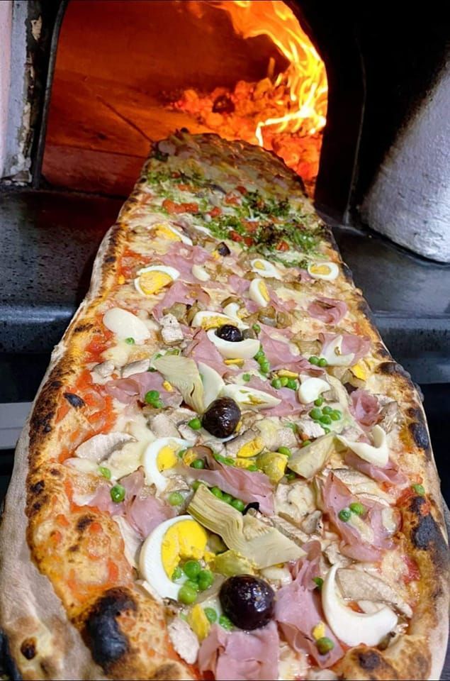 Una pizza molto lunga con molti condimenti viene cotta nel forno.