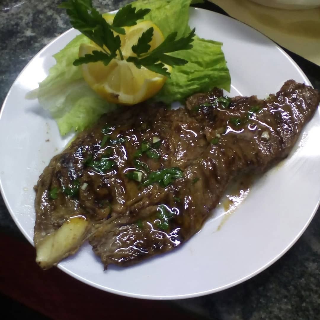 Un piatto bianco sormontato da un pezzo di carne e lattuga