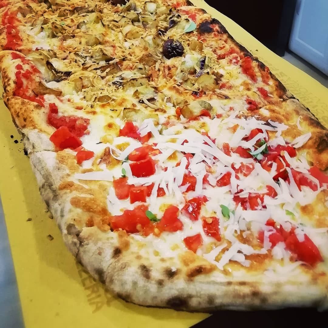 Una pizza con pomodori e formaggio è appoggiata su un tavolo giallo.
