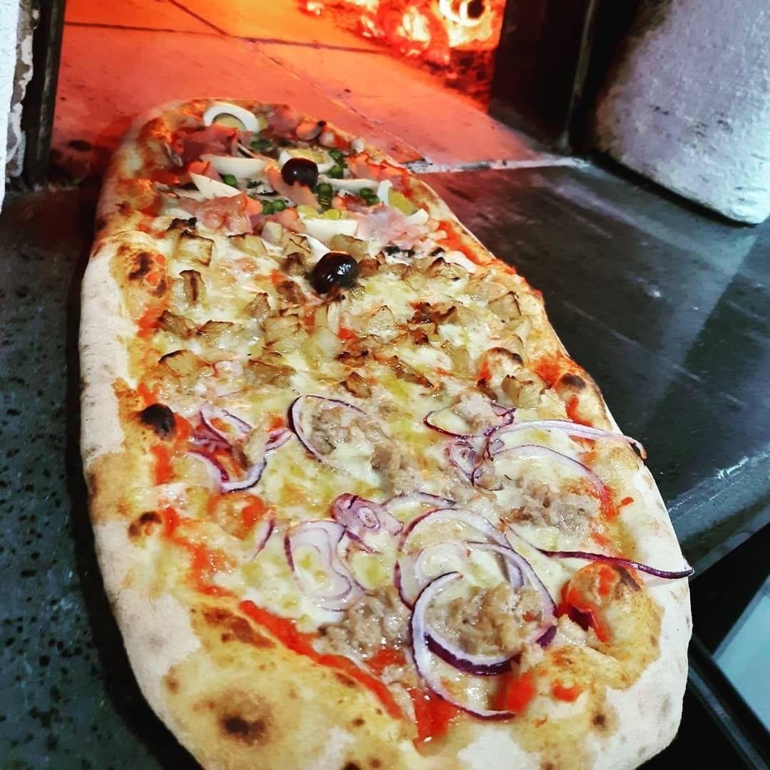 Una pizza lunga è appoggiata su un bancone davanti al forno.