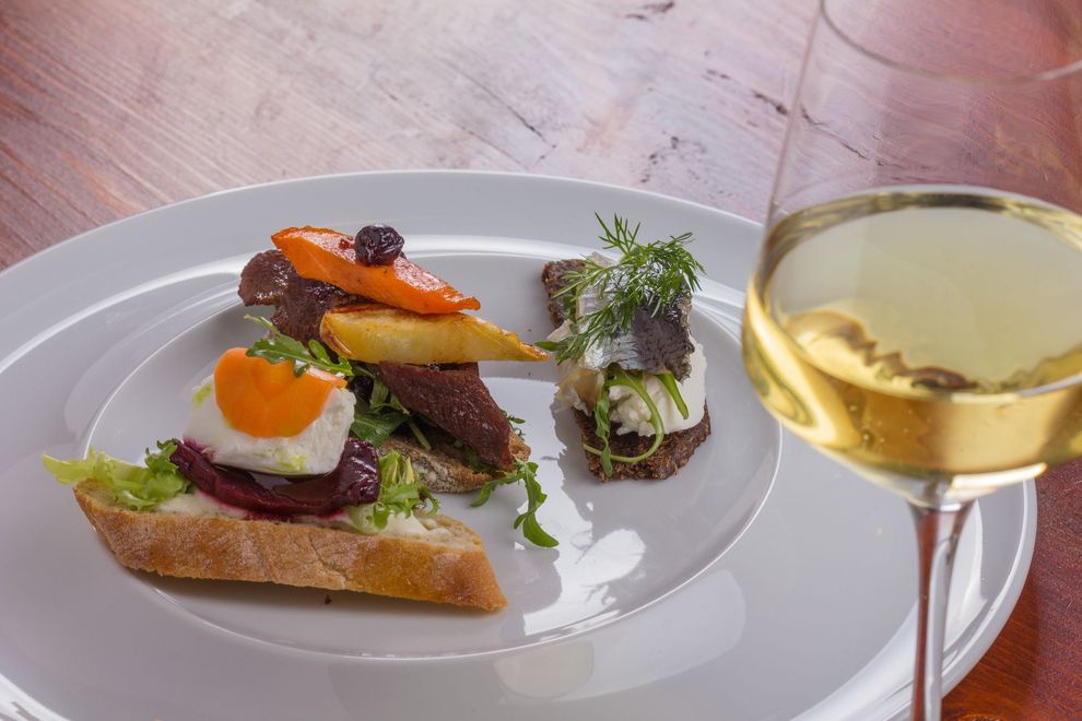 Plated gourmet appetizers beside a glass of white wine on a table