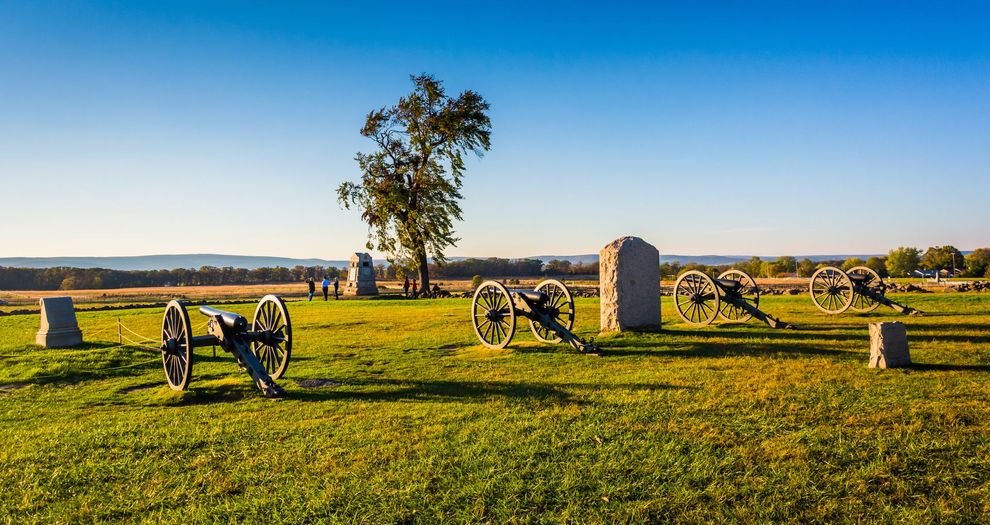 Historic cannons and gravestones in a sunny grassy field with a lone tree and blue sky