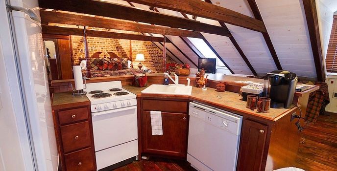 Cozy attic kitchen with wood cabinets, white stove, and sloped beam ceiling, lit by warm lights