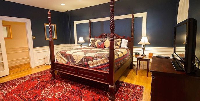 Elegant bedroom with a four-poster bed, red rug, dark walls, and bedside lamps