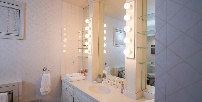 Bright bathroom vanity with mirrors, lights, and a sink with towels hanging on the wall.