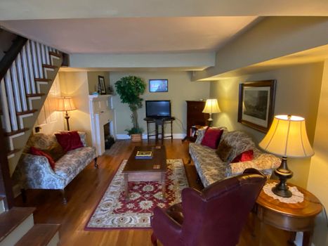 Cozy living room with floral sofas, lamps, wooden floors, and a TV at the back.