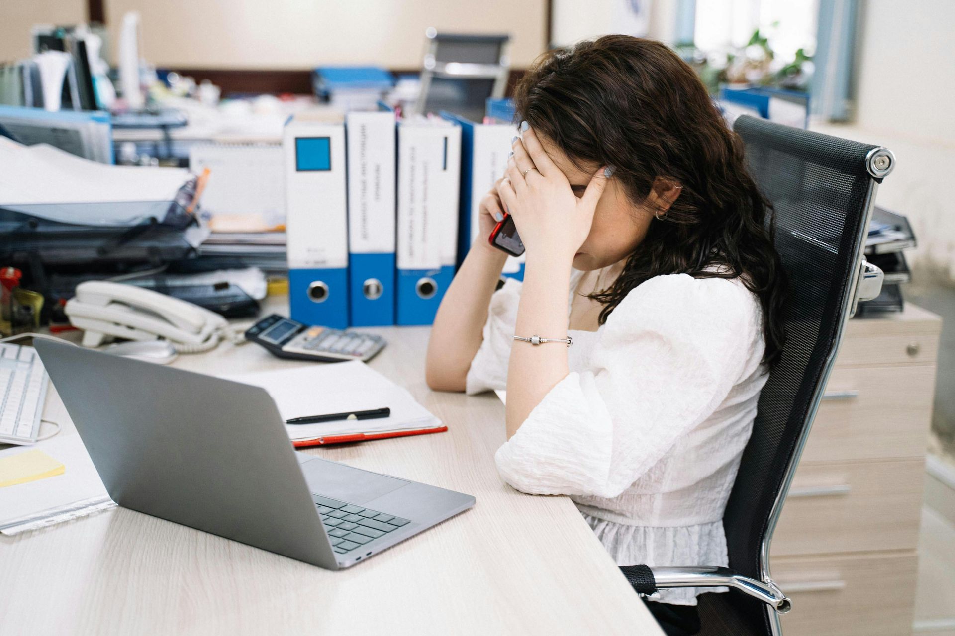 Woman with head in hands at desk, stressed in office setting.