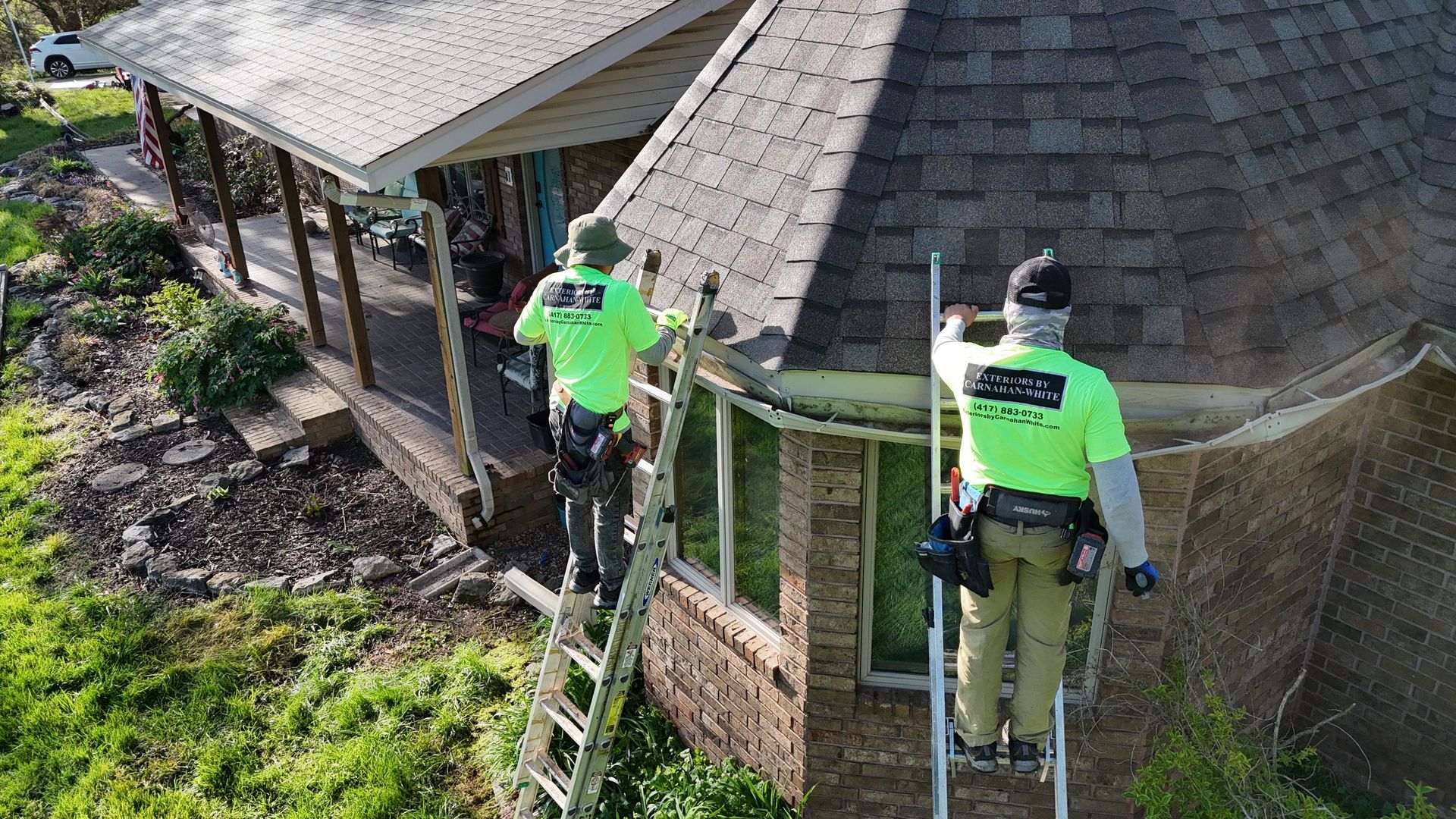 Two men are working on the roof of a house. Gutter replacement nixa mo