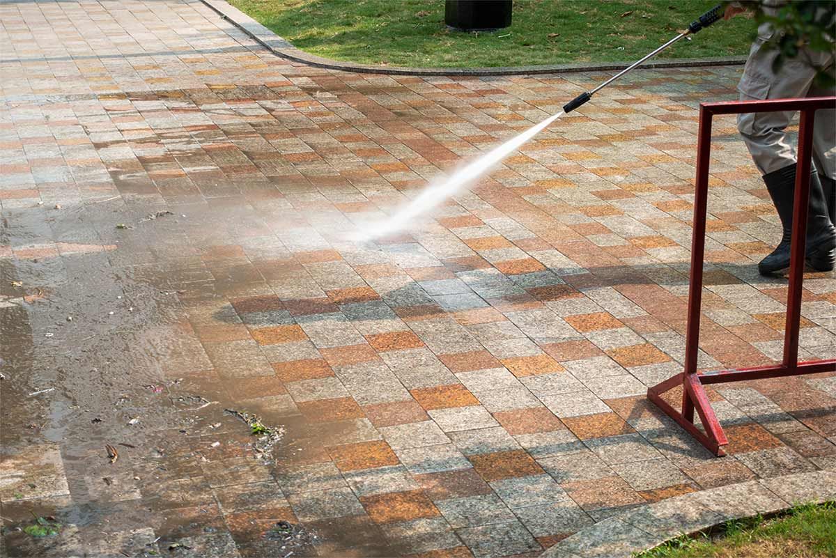 A person is using a high pressure washer to clean a brick walkway.